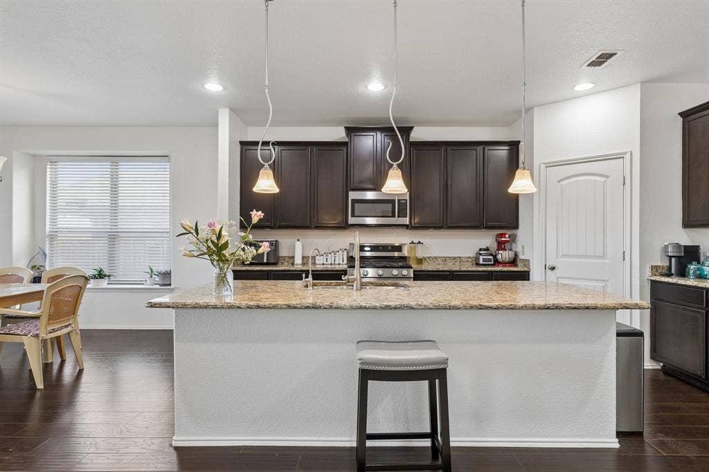 1501 Coyote Ridge Road, Wylie, TX 75098 Kitchen featuring dark wood-finish cabinetry, stainless steel appliances, granite countertops, and a central island with pendant lighting