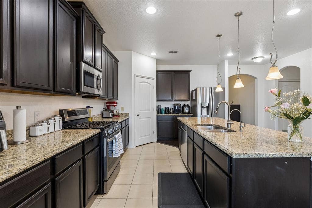 1501 Coyote Ridge Road, Wylie, TX 75098 Kitchen featuring dark wood cabinetry, granite countertops, stainless steel appliances, tile flooring, and pendant lighting