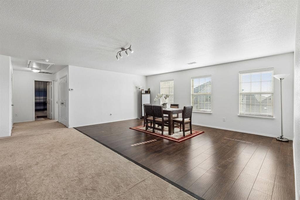 1501 Coyote Ridge Road, Wylie, TX 75098 Spacious open-concept room featuring wood-finish flooring, multiple windows with blinds, track lighting, and neutral wall paint