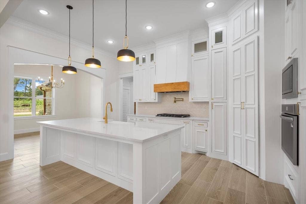 13920 Cedar Hill, Tyler, TX 75704 Bright kitchen featuring white cabinetry, a large center island with a white countertop, wood-finish flooring, and gold-tone fixtures