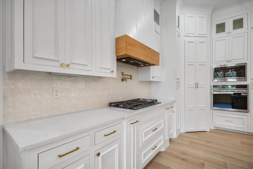 13920 Cedar Hill, Tyler, TX 75704 White cabinetry with gold-finish hardware, light-toned backsplash, gas cooktop, built-in oven, and wood-finish flooring