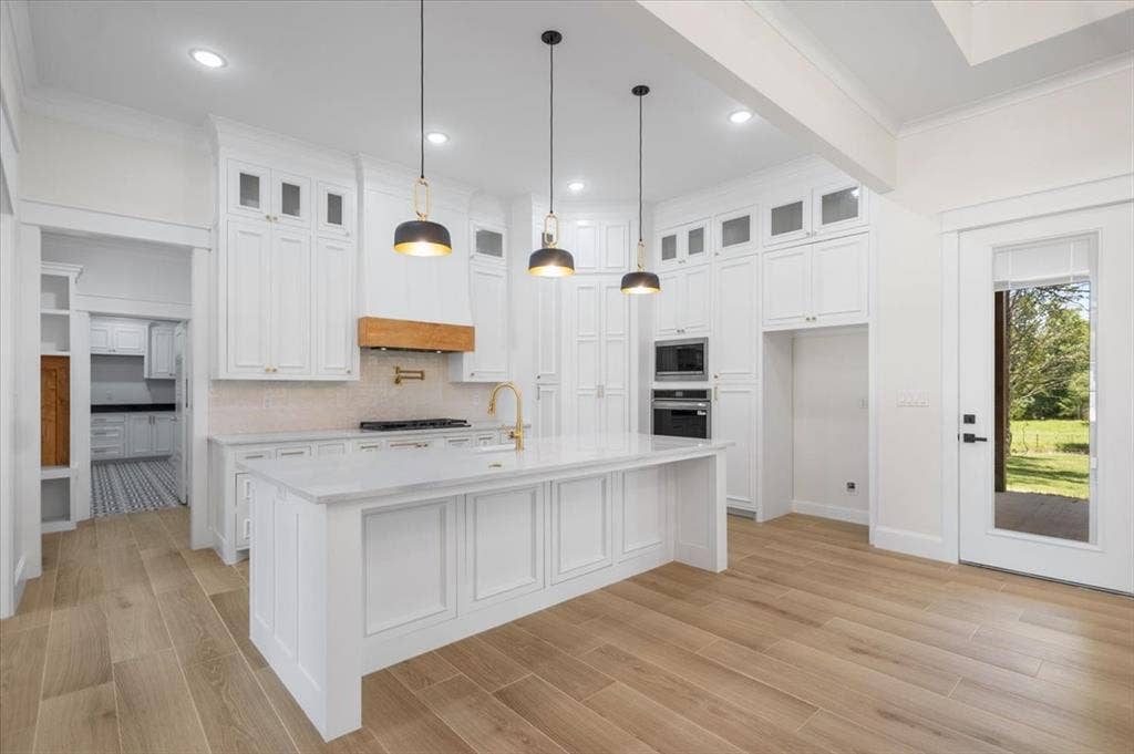 13920 Cedar Hill, Tyler, TX 75704 Spacious kitchen featuring an expansive center island, integrated wall ovens, wood-finish flooring, and white cabinetry with gold-tone hardware
