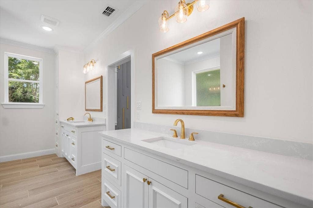 13920 Cedar Hill, Tyler, TX 75704 Dual vanity with white cabinetry and gold-toned hardware, white solid surface countertops, gold-toned wall-mounted lighting, and wood-finish flooring