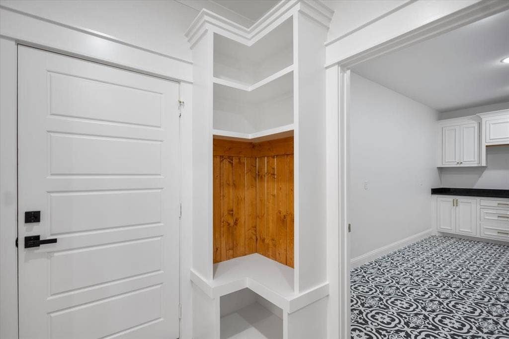 13920 Cedar Hill, Tyler, TX 75704 Built-in shelving with wood paneling, paneled interior door with matte black hardware, white cabinetry, dark countertops, and patterned floor tile