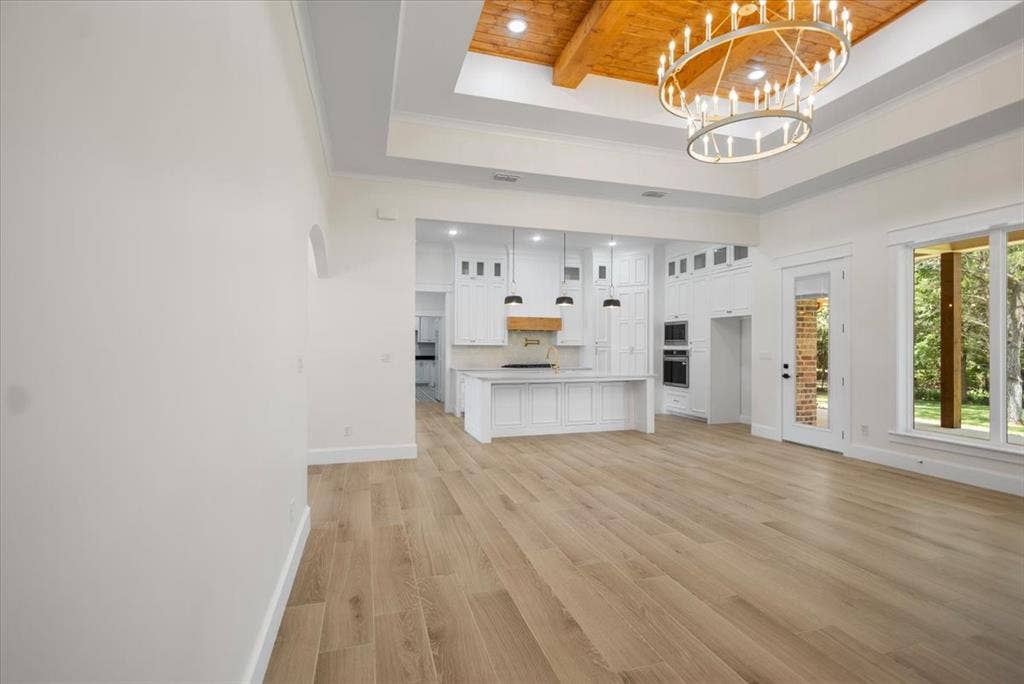 13920 Cedar Hill, Tyler, TX 75704 Wood-finish flooring throughout, tray ceiling with wood-paneled accent, large chandelier, white kitchen cabinetry with island, and large windows