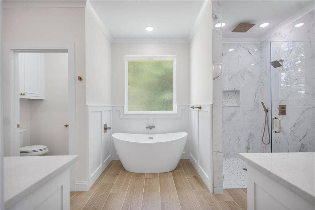 13920 Cedar Hill, Tyler, TX 75704 Freestanding soaking tub, wood-finish flooring, glass-enclosed shower with tiled walls, dual vanity countertops, and wainscoting