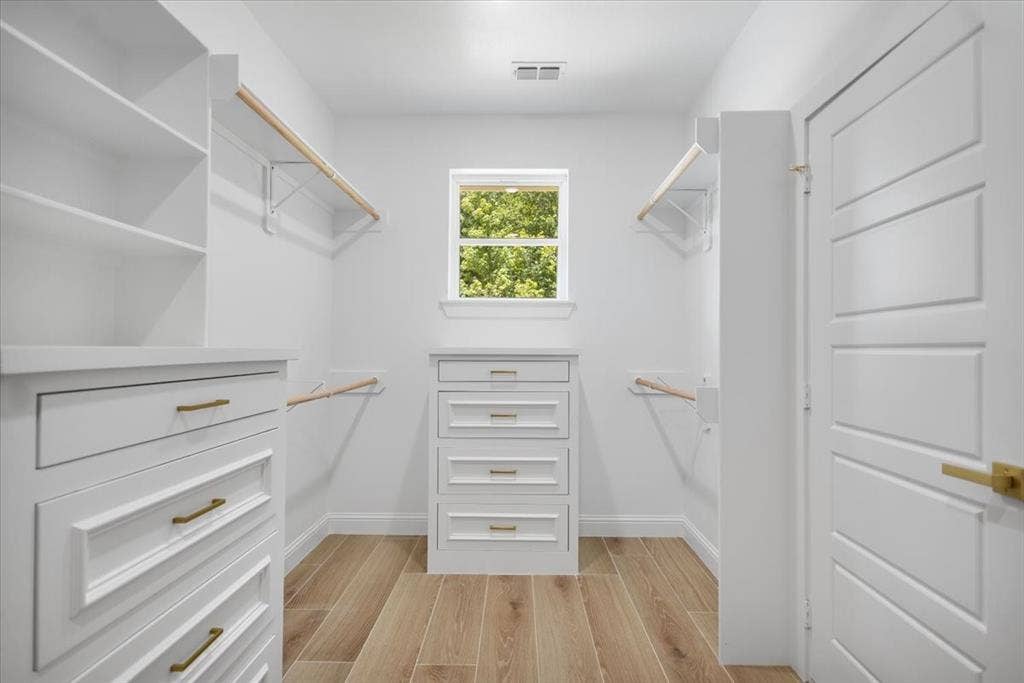 13920 Cedar Hill, Tyler, TX 75704 Spacious walk-in closet featuring wood-finish flooring, built-in shelving, multiple hanging rods, and a window for natural illumination