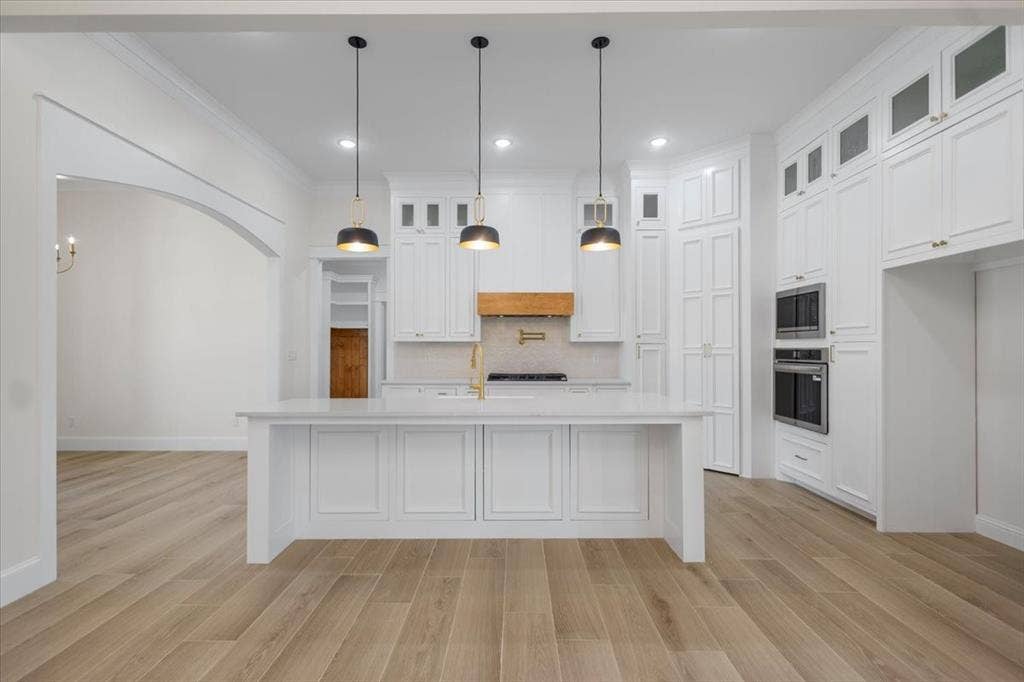 13920 Cedar Hill, Tyler, TX 75704 Expansive kitchen island with a light-toned countertop, integrated double wall ovens, abundant white cabinetry, and wood-finish flooring