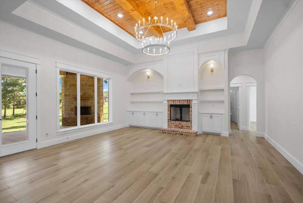 13920 Cedar Hill, Tyler, TX 75704 Wood-finish flooring, a brick fireplace with built-in shelving, tray ceiling with wood paneling, a large chandelier, and expansive windows