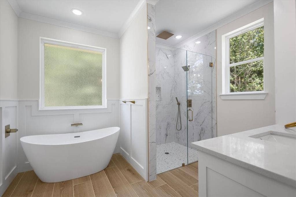 13920 Cedar Hill, Tyler, TX 75704 Freestanding soaking tub, walk-in shower with glass enclosure, wood-finish flooring, white vanity with integrated sink, and recessed lighting