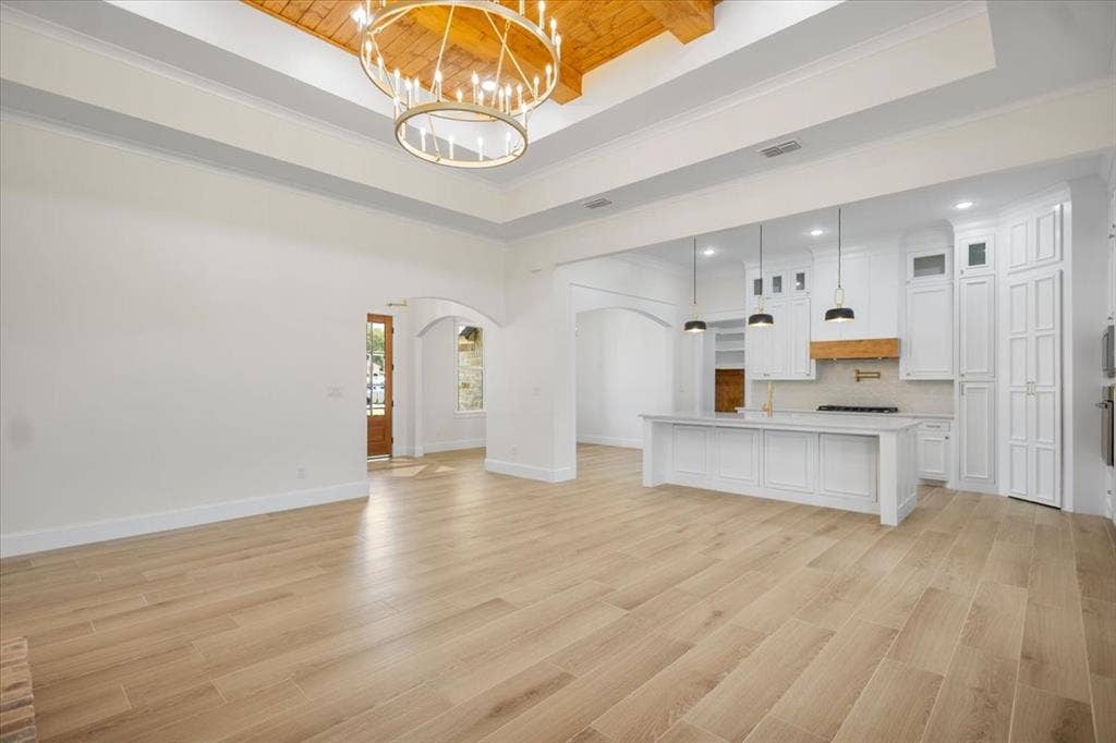 13920 Cedar Hill, Tyler, TX 75704 Expansive open-concept space featuring wood-finish flooring, a tray ceiling with a prominent chandelier, and arched doorways