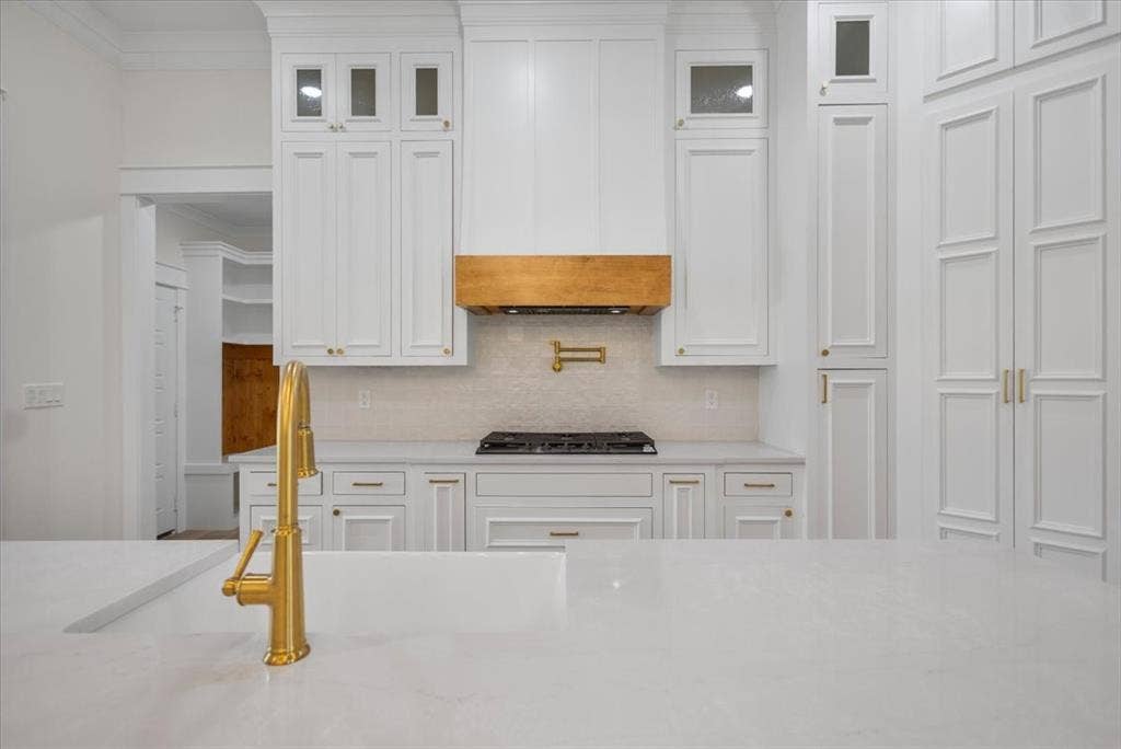 13920 Cedar Hill, Tyler, TX 75704 Expansive countertop with an integrated sink and brass-finish faucet, complemented by white cabinetry, a natural wood-finish range hood, and a gas cooktop