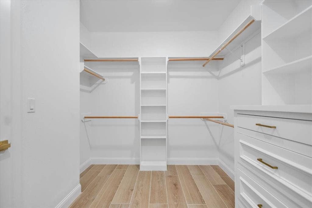 13920 Cedar Hill, Tyler, TX 75704 Custom closet system featuring wood-finish flooring, white built-in shelving, white built-in drawers with gold-tone hardware, and multiple clothing rods