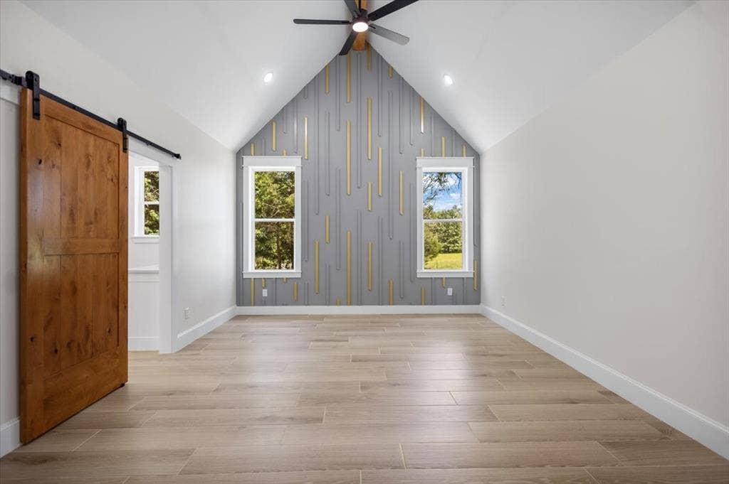 13920 Cedar Hill, Tyler, TX 75704 Vaulted ceiling featuring a ceiling fan, wood-finish flooring, accent wall with vertical paneling, and a wood barn door