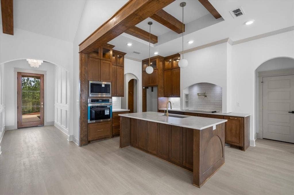17155 Island Lake Dr., Tyler, TX 75708 Gourmet kitchen featuring wood cabinetry, integrated stainless steel appliances, a center island with a sink, and a tile backsplash