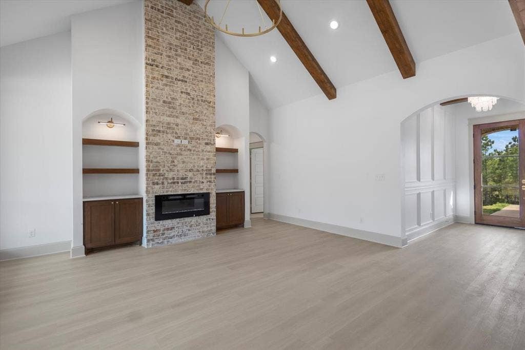 17155 Island Lake Dr., Tyler, TX 75708 Vaulted ceiling with exposed wood beams, brick fireplace with an electric insert, built-in shelving with integrated cabinetry, wood-finish flooring, and an arched entry with wainscoting