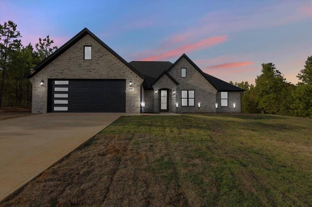 17155 Island Lake Dr., Tyler, TX 75708 Brick exterior with a dark roofline, featuring a concrete driveway and an attached garage with a contemporary door