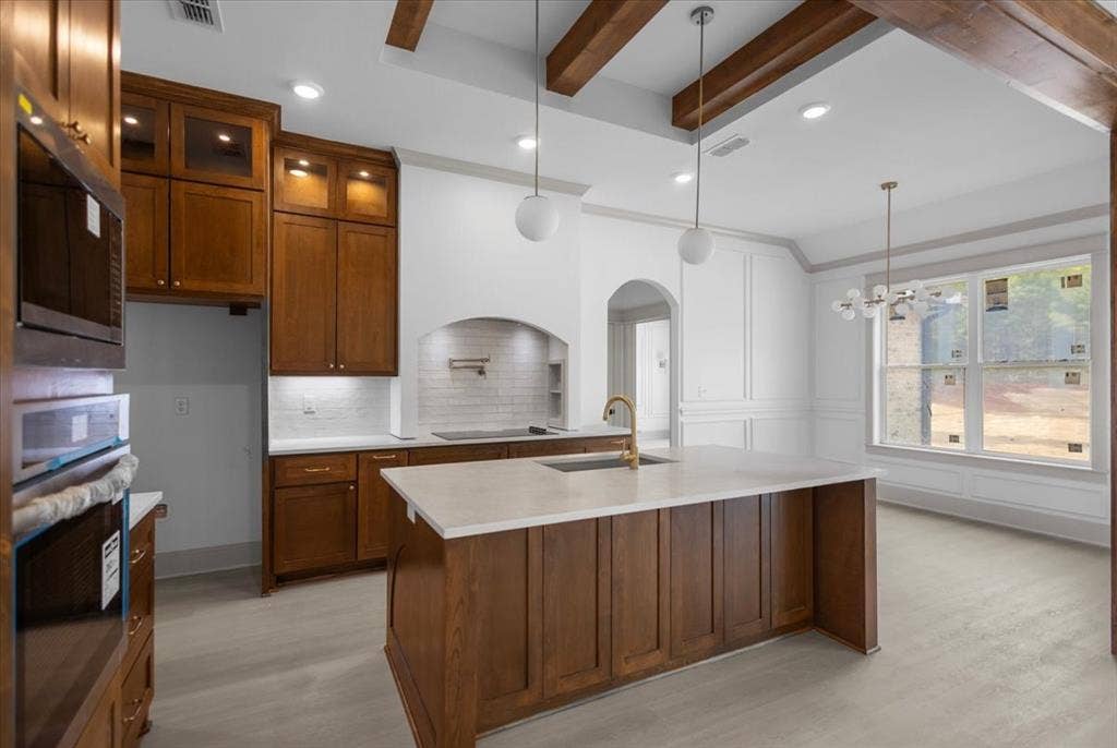 17155 Island Lake Dr., Tyler, TX 75708 Hardwood cabinetry with integrated lighting, a large kitchen island with a light-toned countertop, a tile backsplash, and a decorative arched entryway
