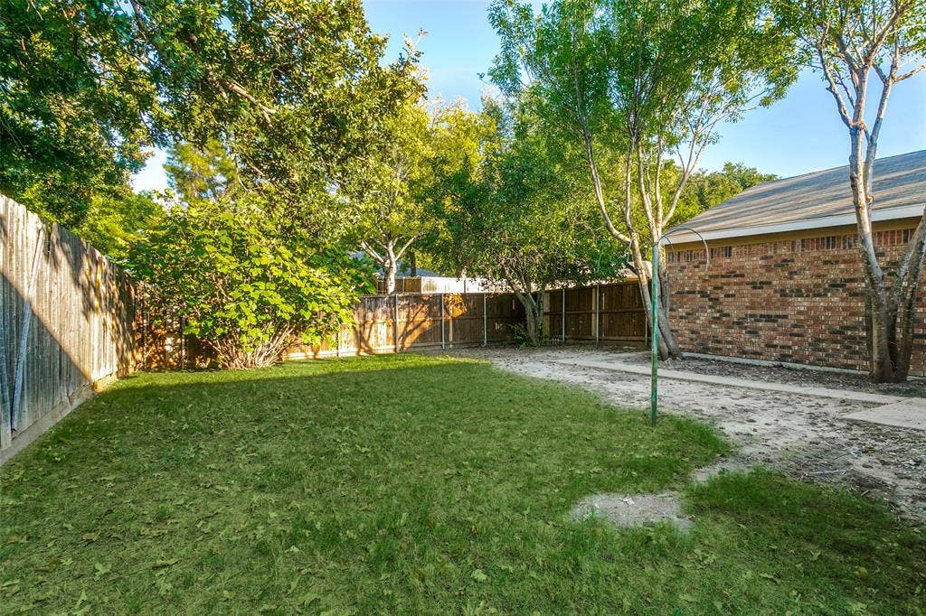 204 Timber Ridge Lane, Coppell, TX 75019 Fenced backyard featuring a lawn area, mature trees, and a brick exterior wall