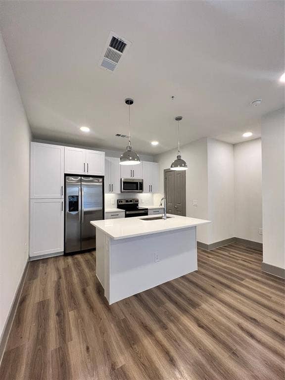 4020 McEwen Road, #9121, Farmers Branch, TX 75244 Kitchen with pendant lighting, appliances with stainless steel finishes, a center island with sink, white cabinets, and dark wood-style flooring