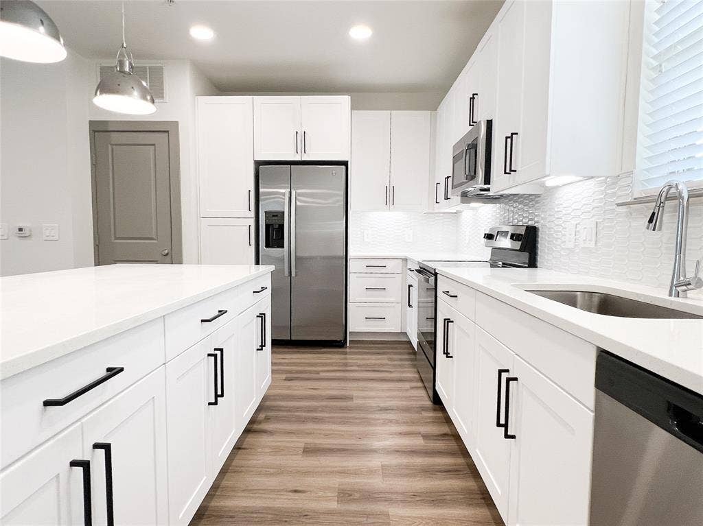4020 McEwen Road, #8115, Farmers Branch, TX 75244 Kitchen featuring stainless steel appliances, white cabinetry, backsplash, light stone countertops, and light wood finished floors