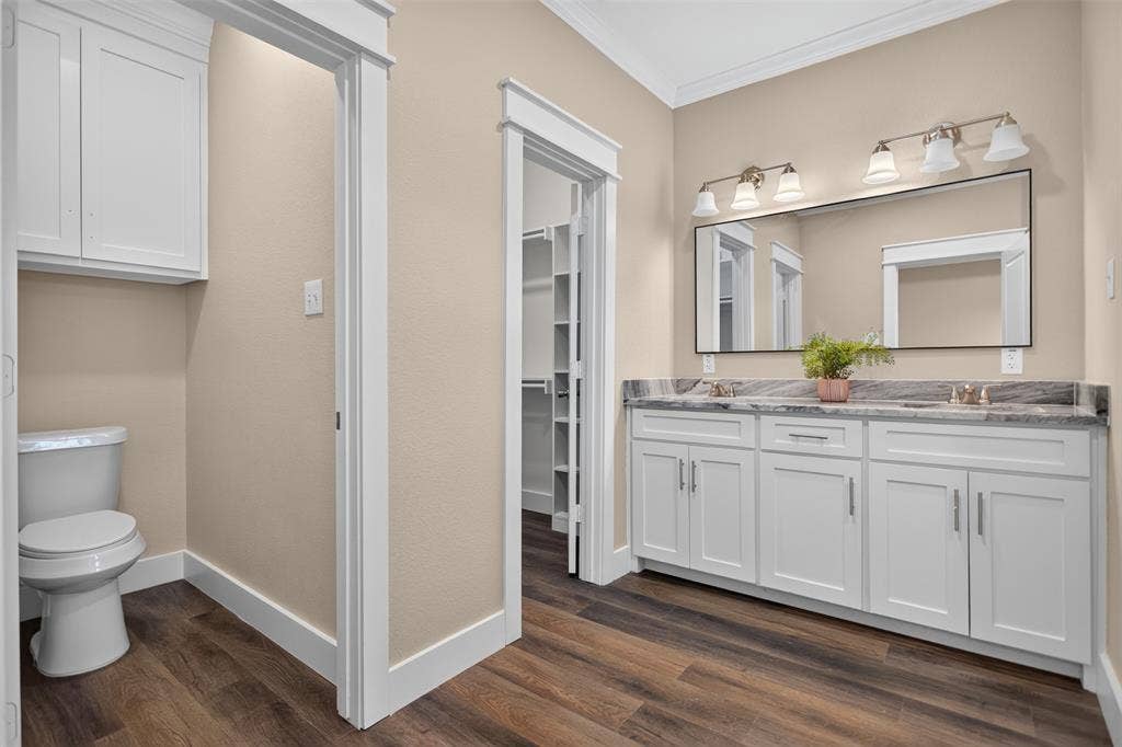 Main Bathroom featuring a white double-sink vanity with stone countertop, large rectangular mirror, multi-bulb wall lighting, and wood-finish flooring
