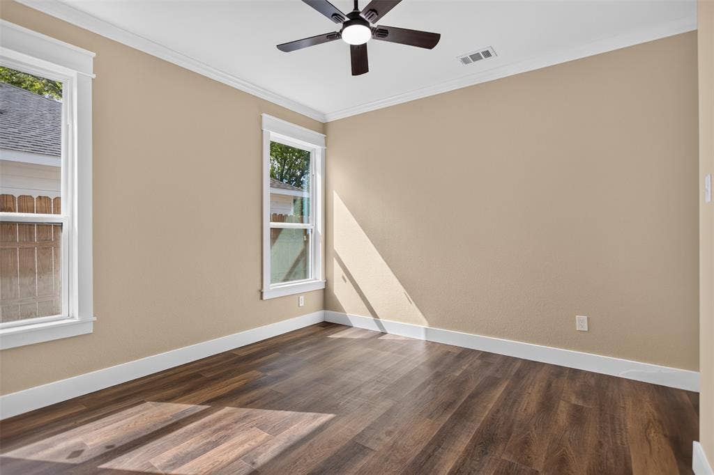 Interior room featuring wood-finish flooring, crown molding, double-pane windows with white trim, and a dark-finish ceiling fan with integrated lighting