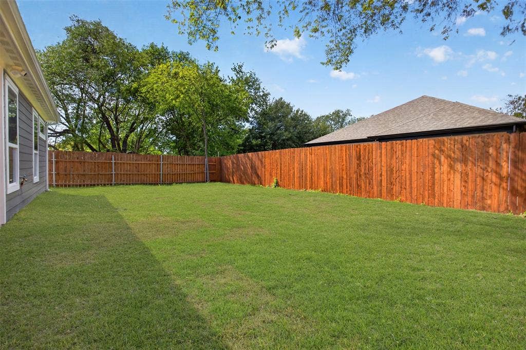 Spacious backyard featuring a manicured lawn, full-perimeter wood fencing, and mature trees