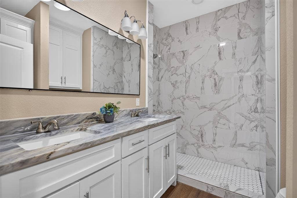 Double vanity with white cabinetry, stone-patterned countertop, under-mount sinks, and a large-format tile walk-in shower with hexagonal floor tiling