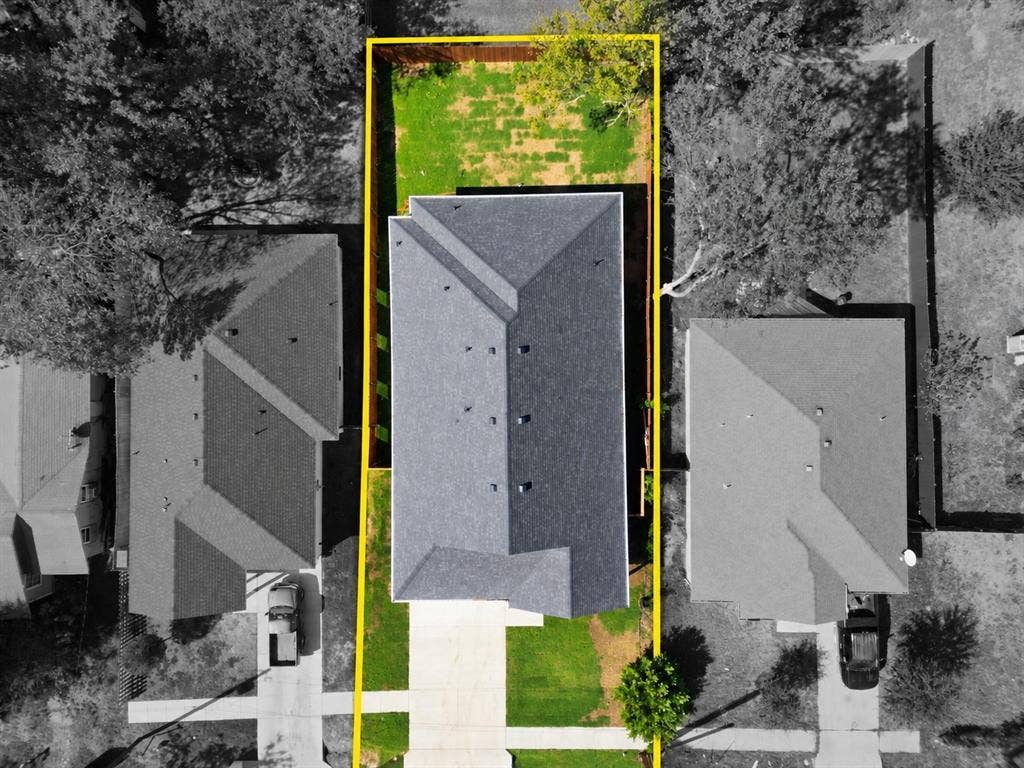 Aerial perspective of the property lot featuring a concrete driveway, multi-gabled roof, and fenced rear yard