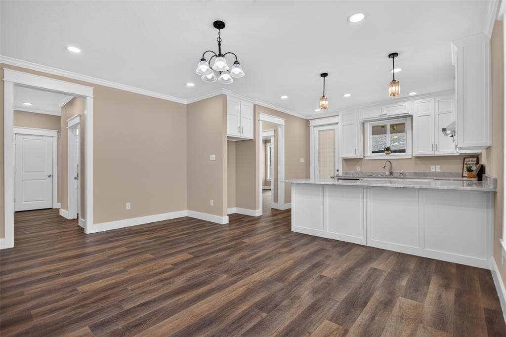Kitchen area featuring white shaker-style cabinetry, granite countertops, a multi-light chandelier, pendant lighting, and wood-finish flooring