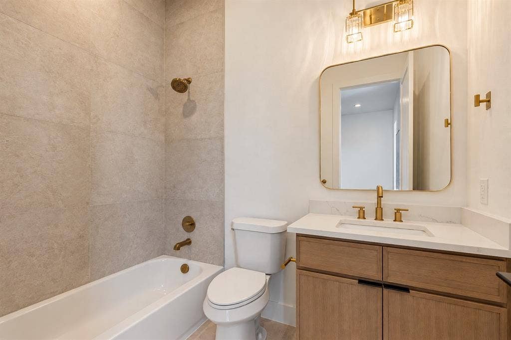 903 Bayonne Street, Dallas, TX 75212 Bathtub with tile surround, toilet, vanity with integrated sink, gold-toned fixtures, and a framed mirror
