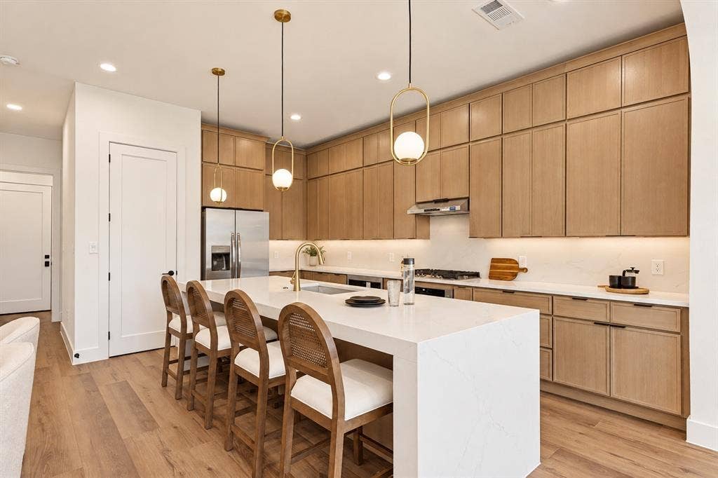 903 Bayonne Street, Dallas, TX 75212 Kitchen featuring light wood-finish cabinetry, a large center island with a white countertop, stainless steel appliances, a gold-tone faucet, and wood-finish flooring