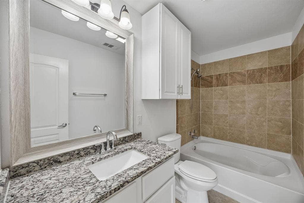 2245 County Road 337, McKinney, TX 75071 Bathroom featuring a vanity with stone-finish countertop, under-mount rectangular sink, framed mirror, wall-mounted cabinetry, and a tub-shower combination with tiled surround