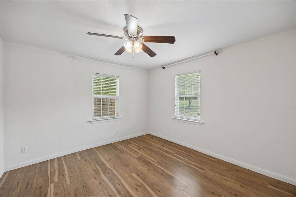2245 County Road 337, McKinney, TX 75071 Neutral interior featuring wood-finish flooring, two double-hung windows with horizontal blinds, and a multi-blade ceiling fan with an integrated light fixture