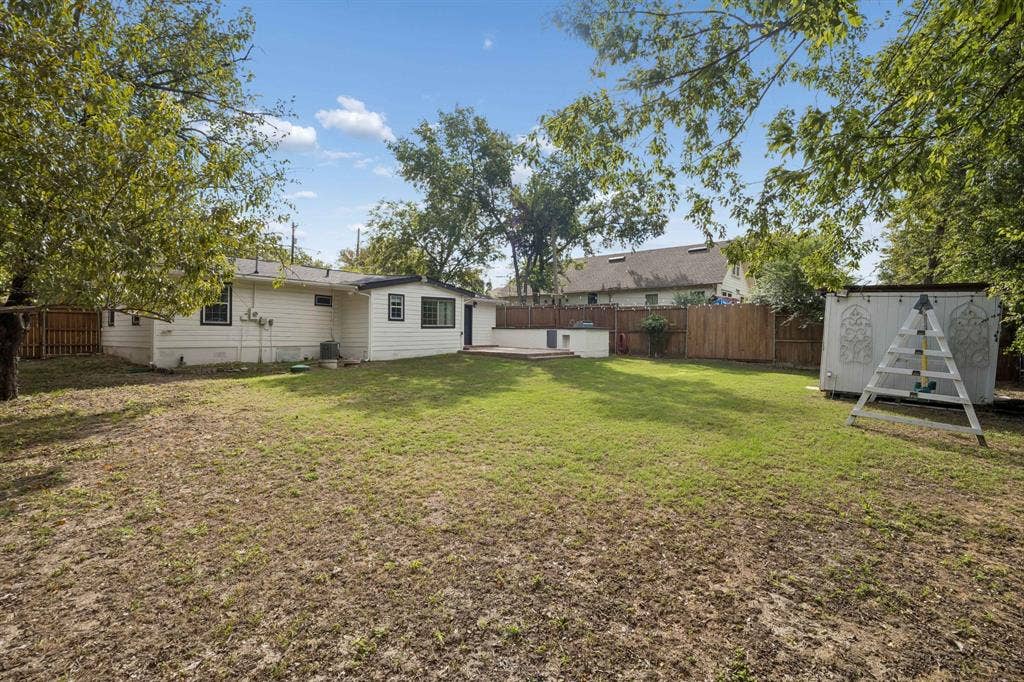 2245 County Road 337, McKinney, TX 75071 Expansive backyard featuring a level lawn, mature trees, a perimeter wood privacy fence, a detached storage structure, and a concrete patio