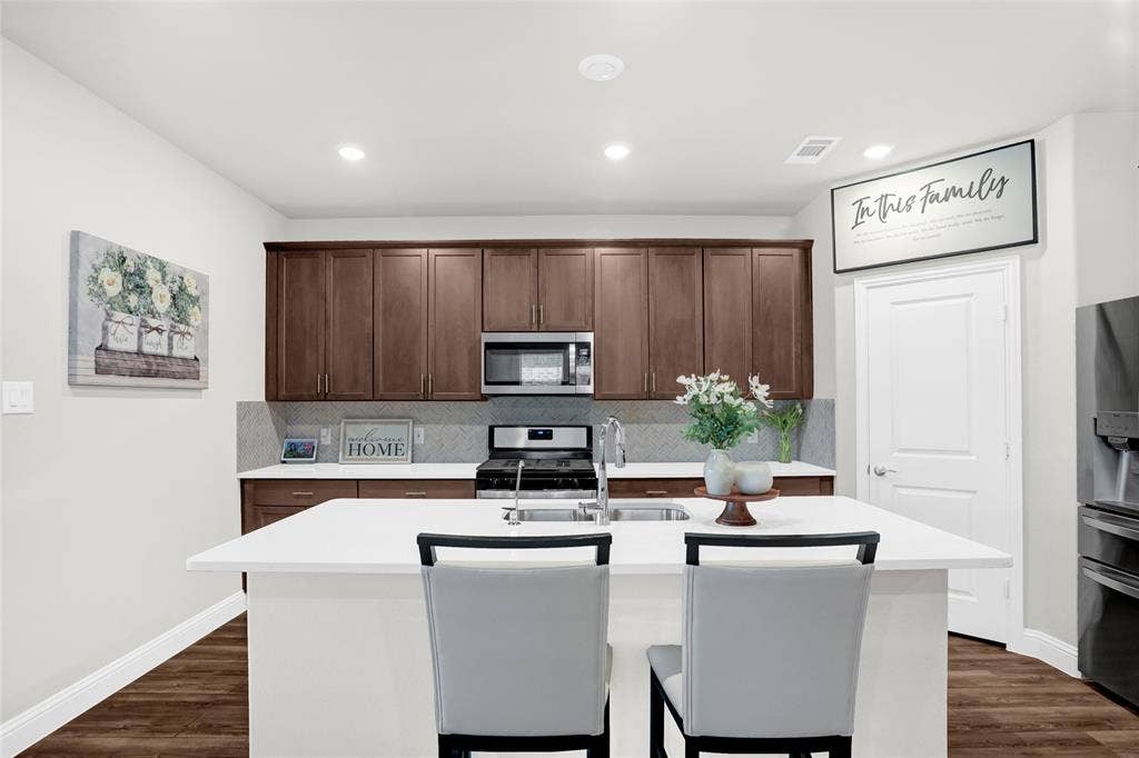 Kitchen with an island with sink, a breakfast bar area, tasteful backsplash, appliances with stainless steel finishes, and dark wood finished floors