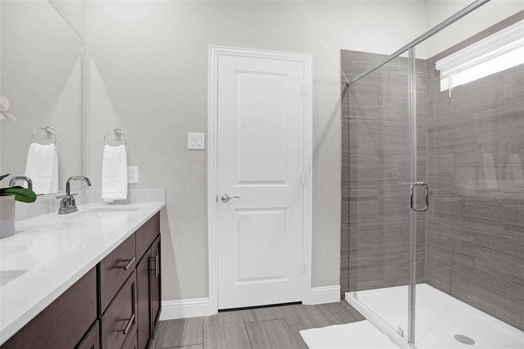 Bathroom featuring double vanity, a shower stall, and light wood-style floors