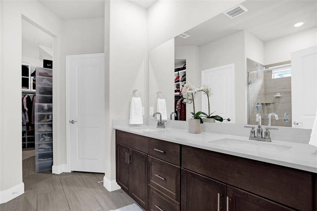 Full bath featuring a spacious closet, a shower stall, double vanity, and light wood-type flooring