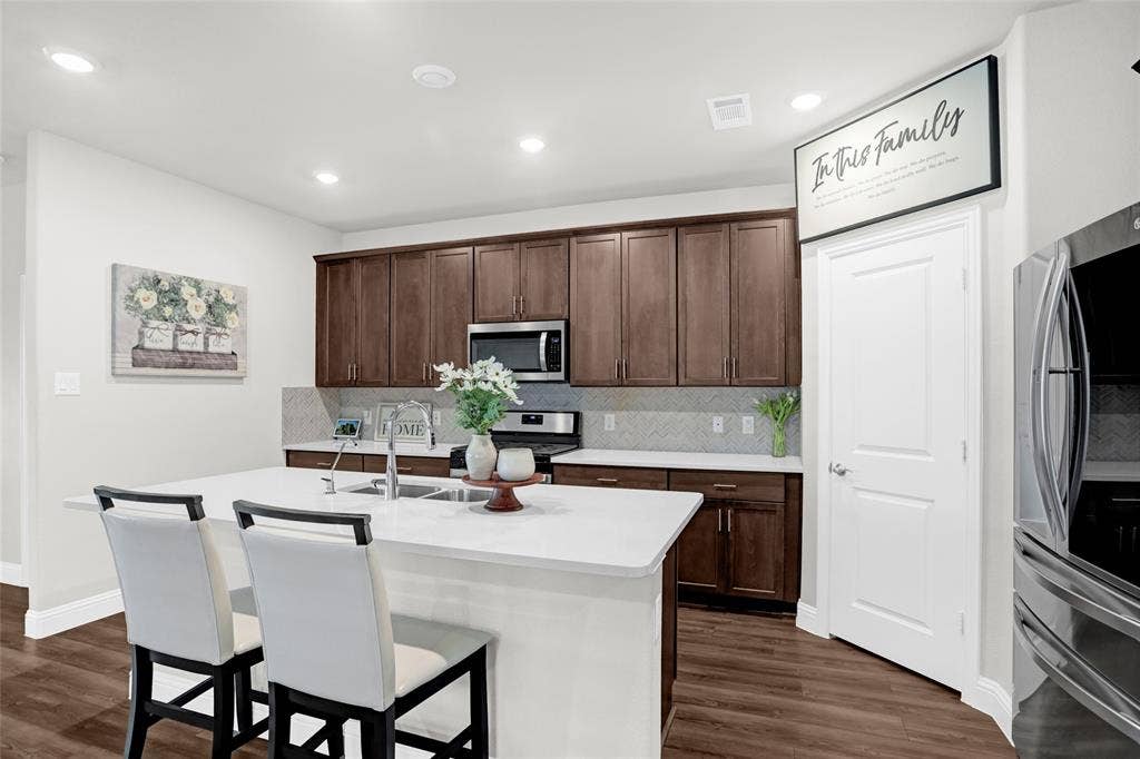 Kitchen with tasteful backsplash, dark wood-type flooring, a kitchen breakfast bar, stainless steel appliances, and recessed lighting