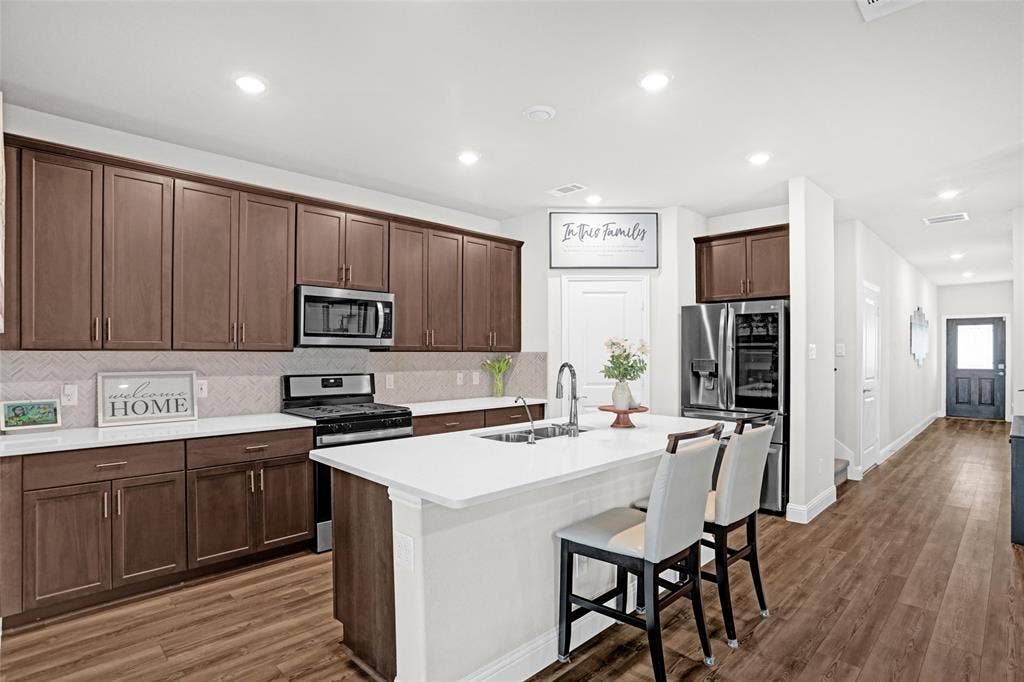 Kitchen featuring decorative backsplash, stainless steel appliances, a breakfast bar area, recessed lighting, and dark wood-type flooring