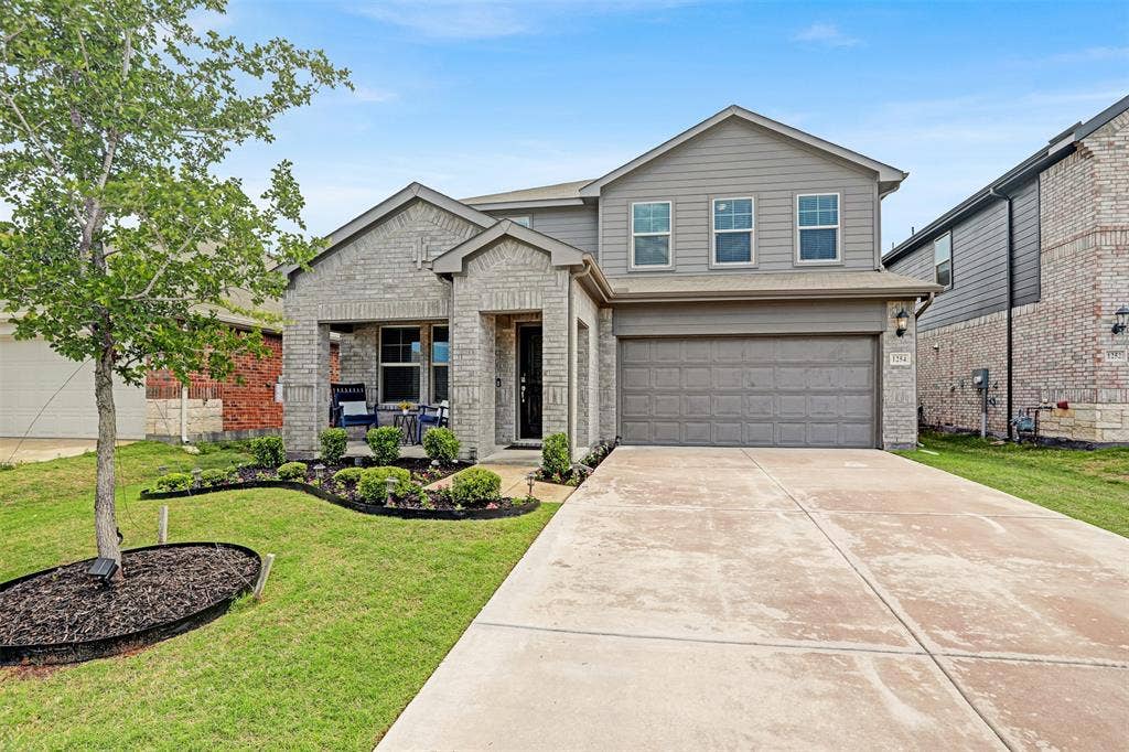 Traditional-style home featuring an attached garage, brick siding, driveway, and a front lawn