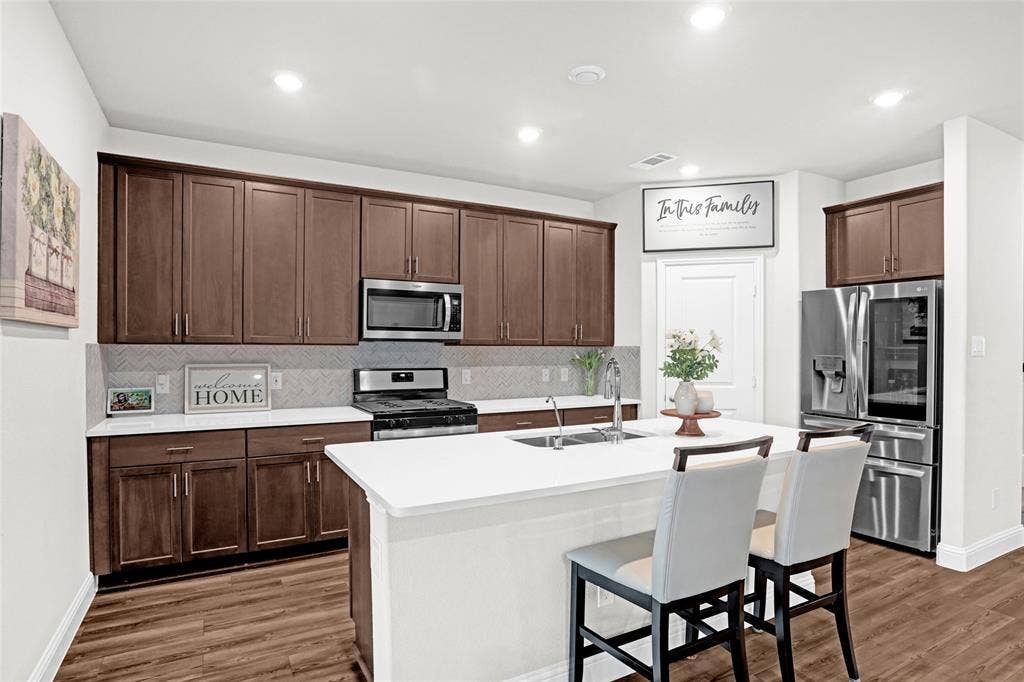 Kitchen with backsplash, stainless steel appliances, a breakfast bar, a center island with sink, and recessed lighting