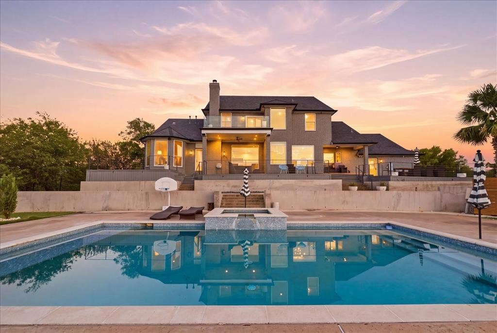 2945 Emerald Sound Drive, Cedar Hill, TX 75104 Rear exterior featuring a swimming pool with a spillover spa, multi-level concrete decking, a second-story glass-railed balcony, and a prominent exterior chimney