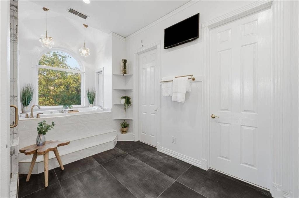 2945 Emerald Sound Drive, Cedar Hill, TX 75104 Soaking tub with a tiled surround, arched window, dark tile flooring, built-in corner shelving, and dual glass pendant lighting