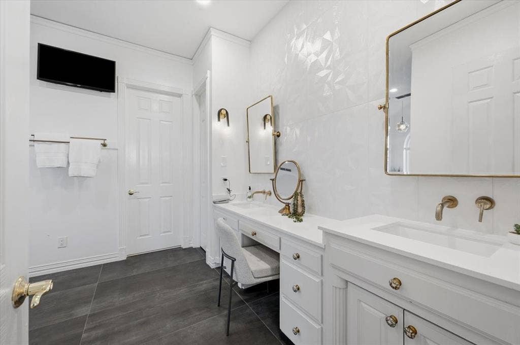 2945 Emerald Sound Drive, Cedar Hill, TX 75104 Custom white cabinetry with integrated vanity, textured white wall tiling, gold-tone hardware, rectangular undermount sinks, and dark tile flooring
