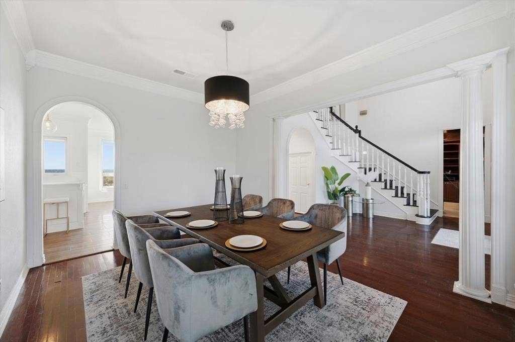 2945 Emerald Sound Drive, Cedar Hill, TX 75104 Formal dining area featuring dark wood-finish flooring, a contemporary drum chandelier with crystal accents, crown molding, arched entryways, and a staircase with a black handrail and white balusters