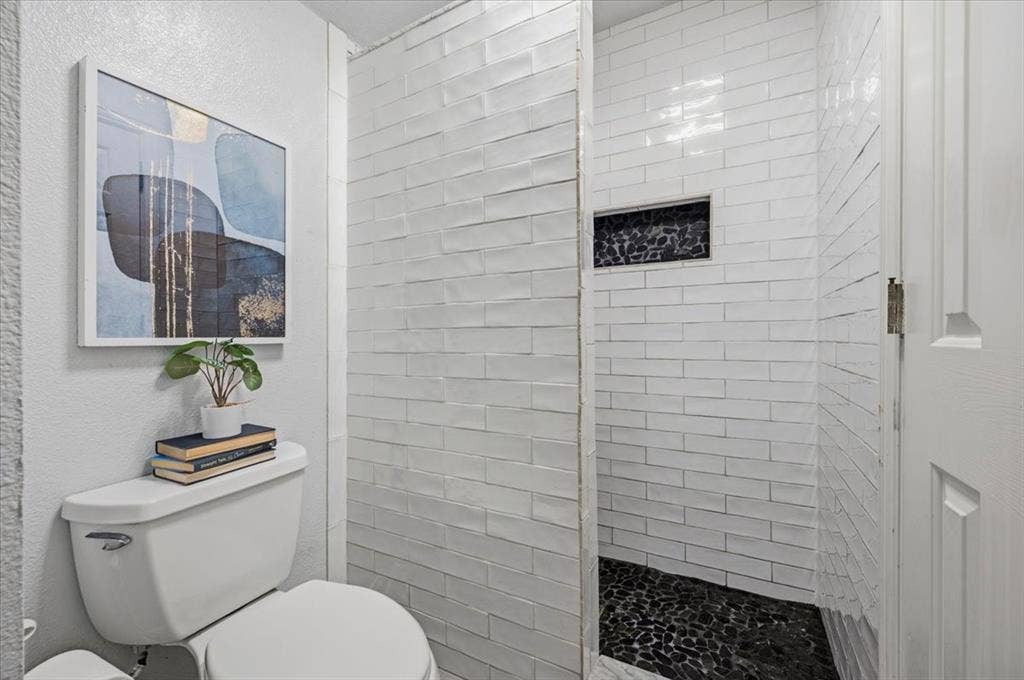 2945 Emerald Sound Drive, Cedar Hill, TX 75104 Walk-in shower featuring white subway tile, dark pebble-stone flooring, and a recessed tiled niche