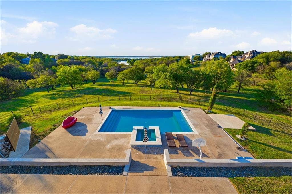 2945 Emerald Sound Drive, Cedar Hill, TX 75104 In-ground swimming pool with an attached spa, expansive concrete patio, metal perimeter fencing, and mature trees across a multi-acre landscape