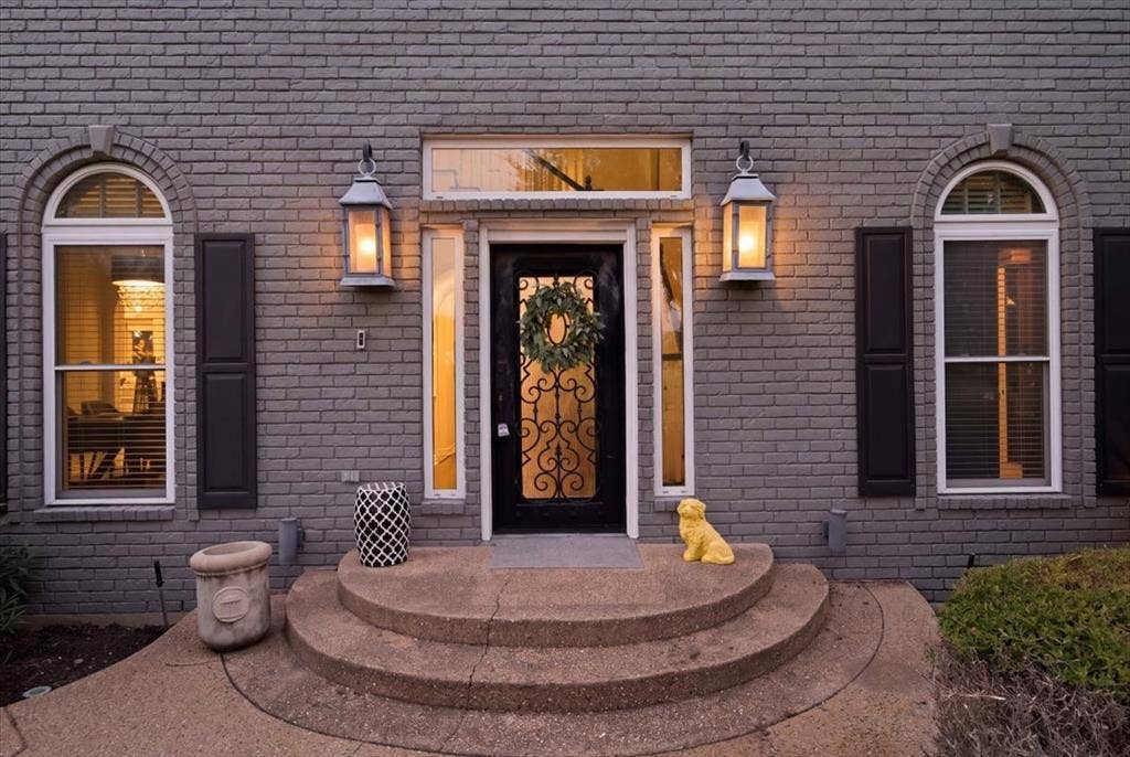 2945 Emerald Sound Drive, Cedar Hill, TX 75104 Gray brick exterior featuring a decorative iron-glass entry door, arched windows with shutters, dual exterior lanterns, and a curved concrete stoop with a transom window